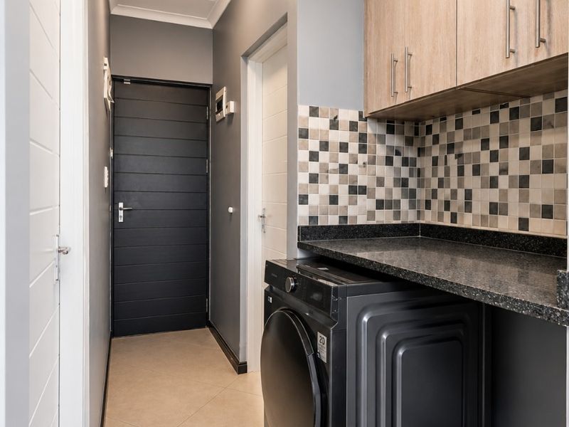 A well-maintained laundry area featuring built-in wooden cabinetry, a dark granite countertop, mosaic tile backsplash, and tiled flooring.