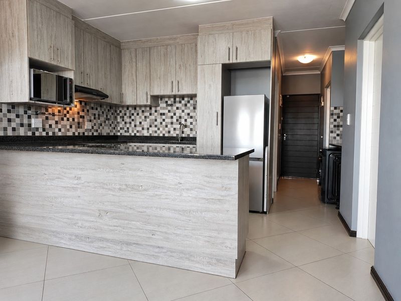 Modern kitchen featuring light wood-look cabinetry, granite countertops, mosaic tile backsplash, and a functional breakfast bar layout.