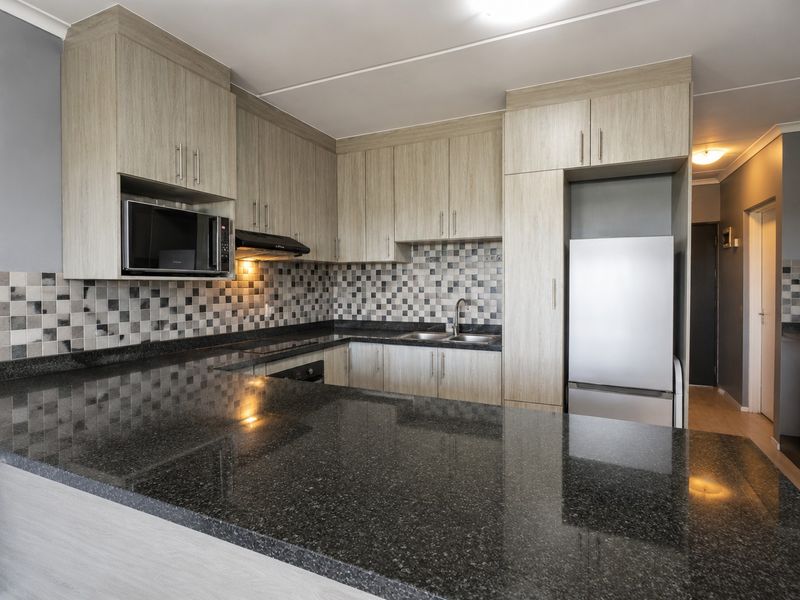 Modern kitchen featuring light wood-grain cabinetry, dark granite countertops, a mosaic tile backsplash, and integrated appliances including an oven and microwave.