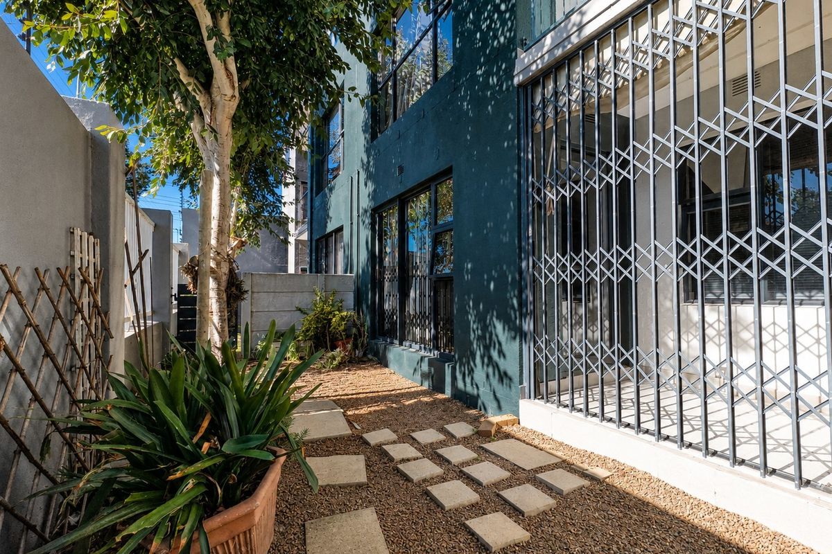 A private rear courtyard area featuring gravel ground cover, stone pavers, and a secure metal gate entrance to the apartment.