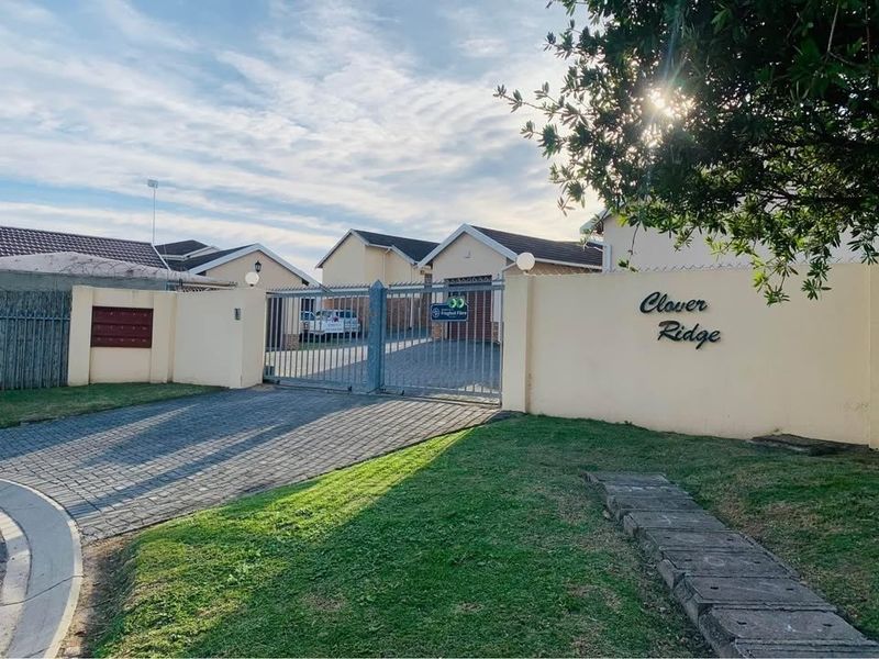 Front entrance view of Clover Ridge townhouse complex featuring a secure gated access point, paved driveway, and perimeter walling.