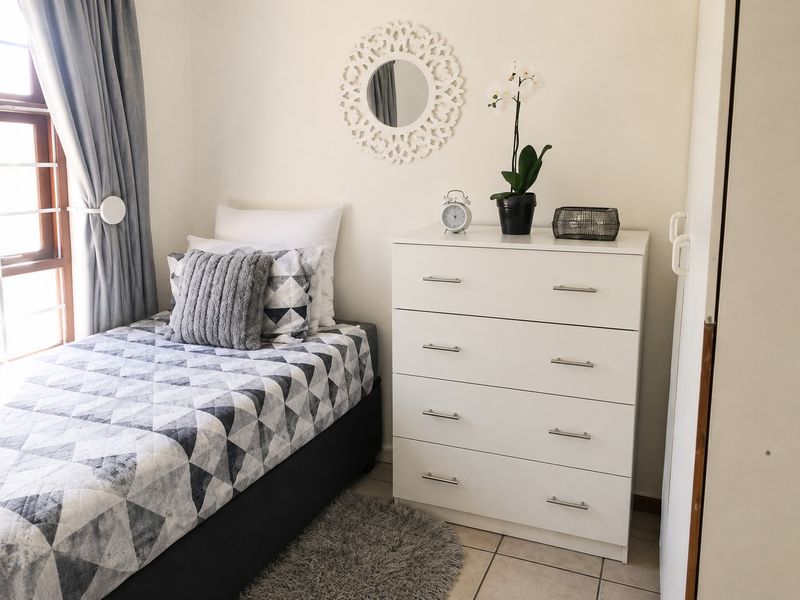 A compact bedroom featuring tiled flooring and a window fitted with security bars, providing natural light and a functional layout.