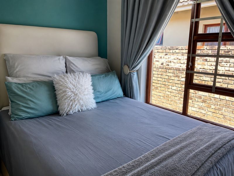 A cozy bedroom featuring a teal accent wall and a large timber-framed window with security bars, overlooking an exterior brick wall.