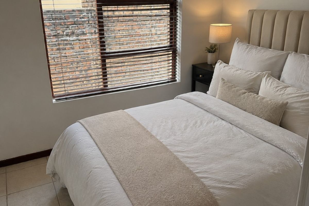 A cozy bedroom featuring neutral tiled flooring and a window fitted with venetian blinds, offering a simple and functional living space.