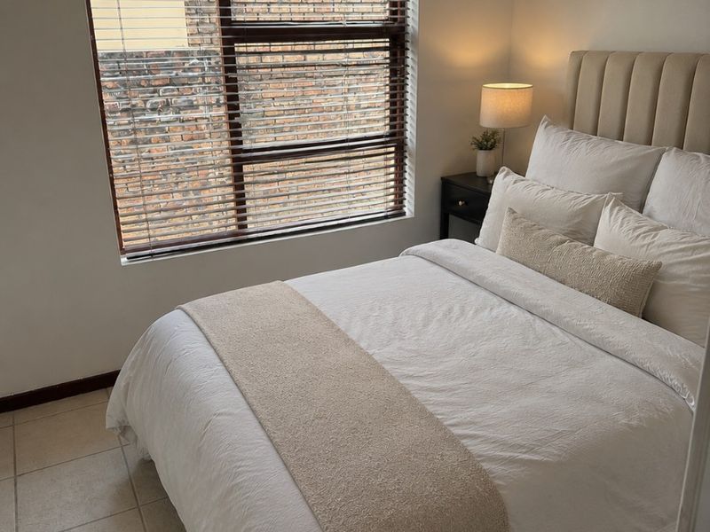A cozy bedroom featuring neutral tiled flooring and a window fitted with venetian blinds, offering a simple and functional living space.