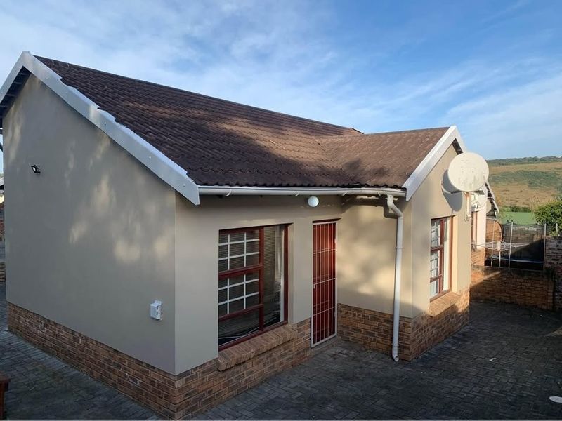 Rear view of the townhouse featuring a tiled roof, brick base detailing, security gate, and paved courtyard area.