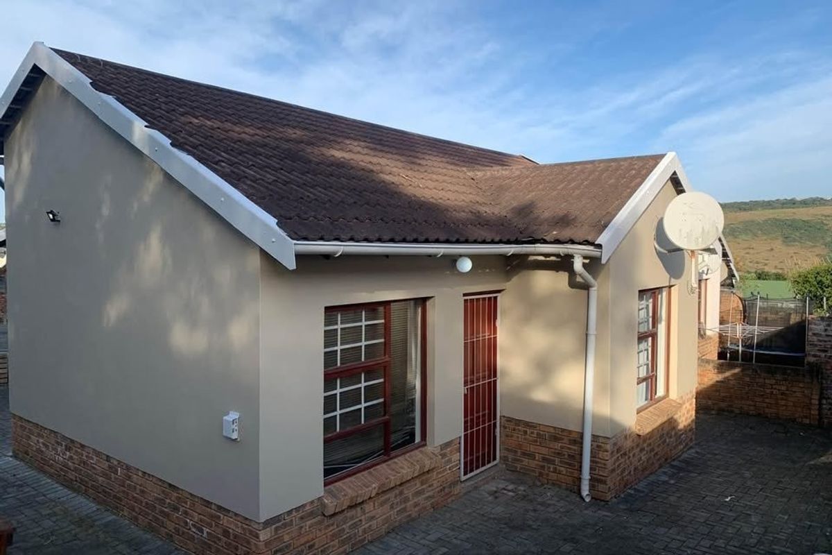 Rear view of the townhouse featuring a tiled roof, brick base detailing, security gate, and paved courtyard area.