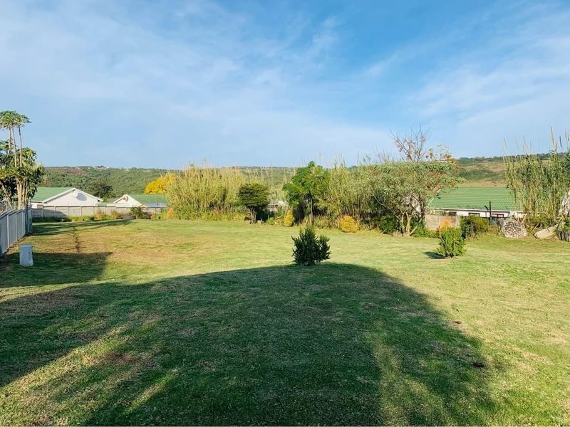 A spacious, open grass garden area with perimeter fencing and surrounding greenery.