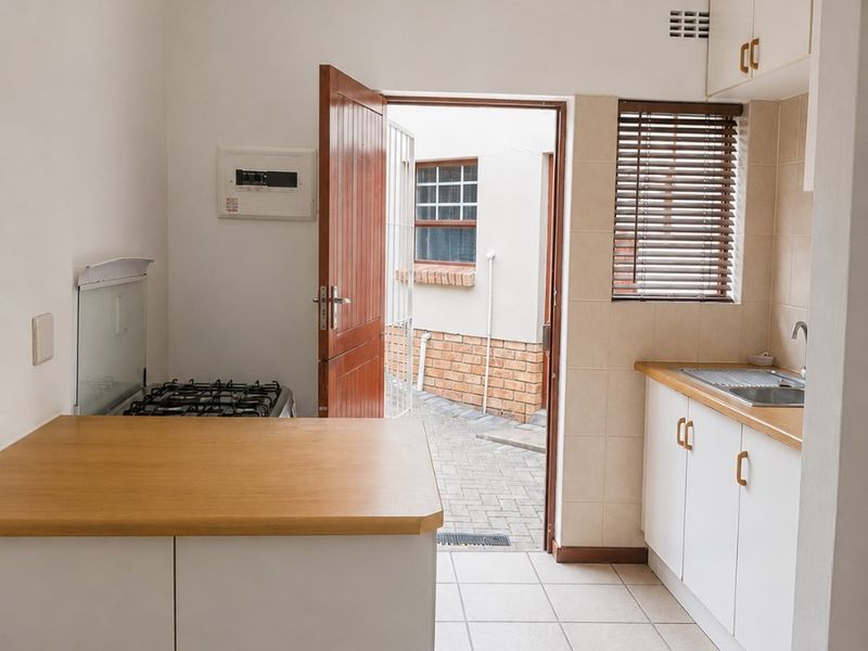 A compact, functional kitchen featuring white cabinetry, laminate countertops, a gas hob, and direct access to an outdoor courtyard area.