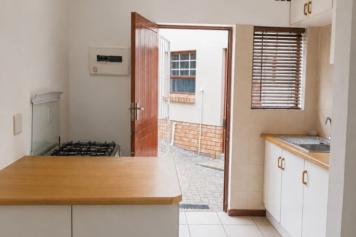 A compact, functional kitchen featuring white cabinetry, laminate countertops, a gas hob, and direct access to an outdoor courtyard area.
