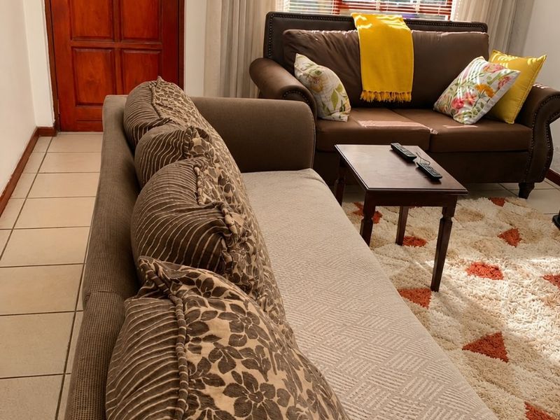 A living room area featuring tiled flooring, a timber entrance door, and natural light filtered through venetian blinds.