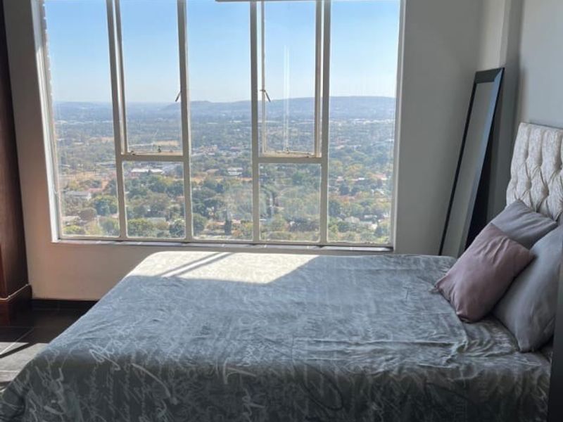 A bright bedroom featuring a ceiling fan, tiled flooring, and a large window offering expansive elevated views.