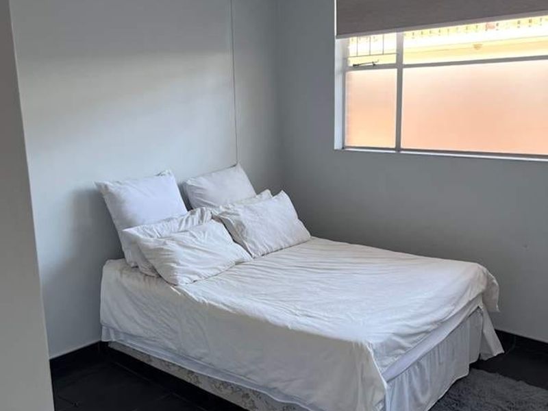 A simple bedroom featuring tiled flooring, a roller blind, and a central pendant light fixture.