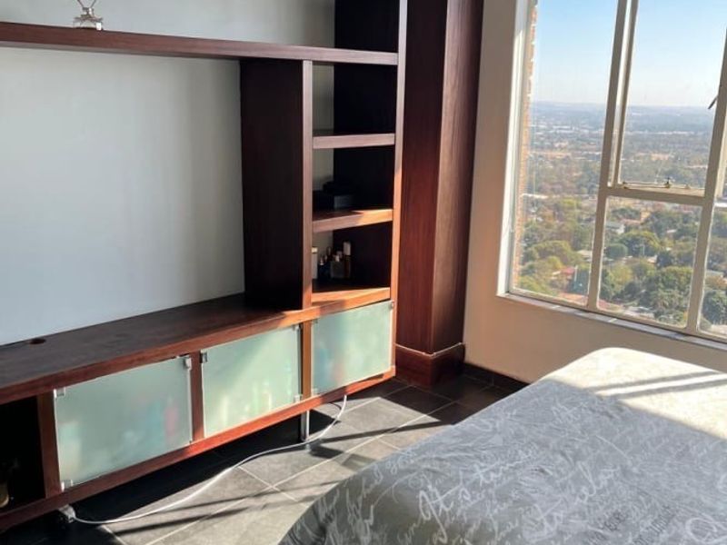 A bright bedroom featuring dark tiled flooring, a large window with expansive views, and a custom built-in wooden shelving and storage unit.