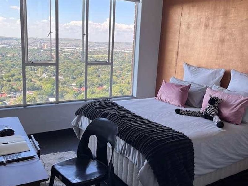 A bright bedroom featuring a large picture window with expansive views, a ceiling fan, and a feature wall.