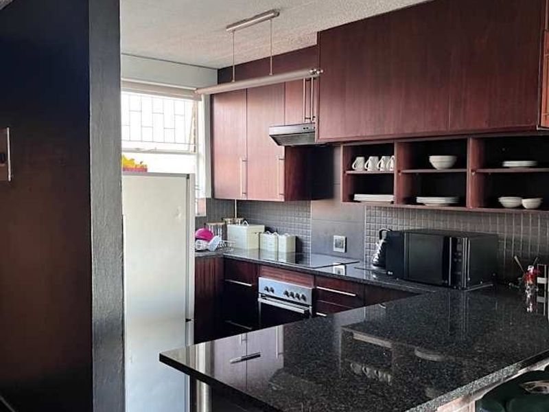A functional kitchen featuring dark wood cabinetry, granite countertops, a breakfast bar with a brick base, and integrated cooking appliances.
