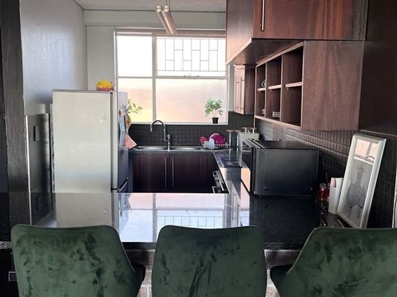 A compact kitchen featuring dark wood cabinetry, black granite countertops, and a brick-style breakfast bar, offering a functional and modern aesthetic.