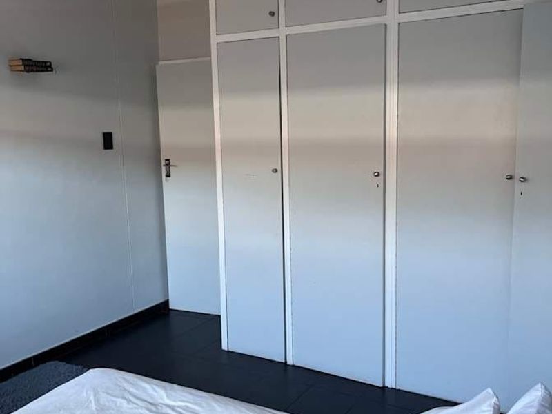 A bedroom featuring built-in cupboards with overhead storage, tiled flooring, and a central pendant light fixture.
