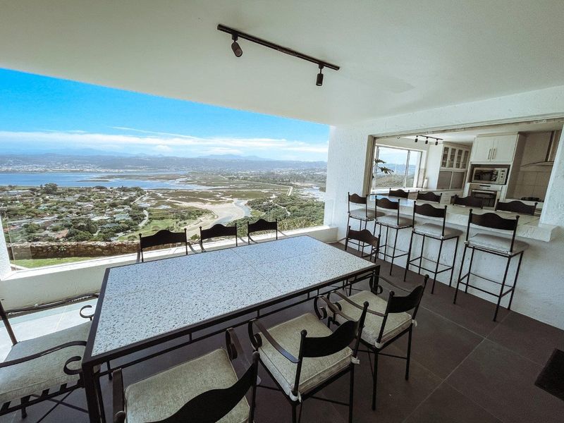Spacious covered patio featuring a stone breakfast bar, track lighting, and expansive panoramic views of the surrounding landscape and estuary.