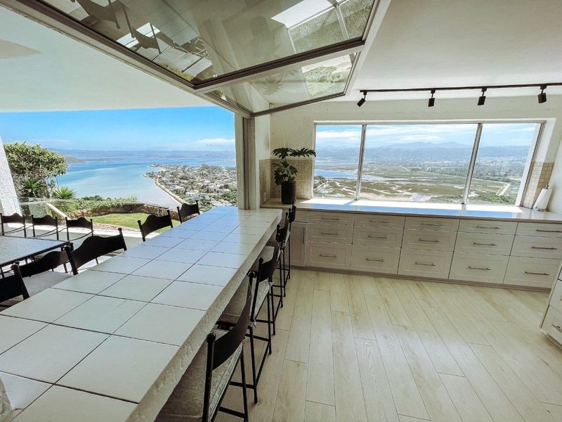 Modern kitchen featuring a tiled breakfast bar, extensive built-in cabinetry, and a retractable glass wall offering panoramic coastal and landscape views.