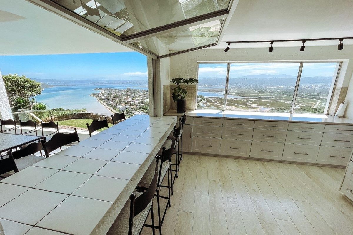 Modern kitchen featuring a tiled breakfast bar, extensive built-in cabinetry, and a retractable glass wall offering panoramic coastal and landscape views.