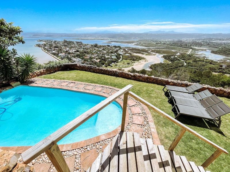 Elevated outdoor pool area featuring a stone-paved surround, retaining wall, and expansive panoramic views of the lagoon and surrounding landscape.