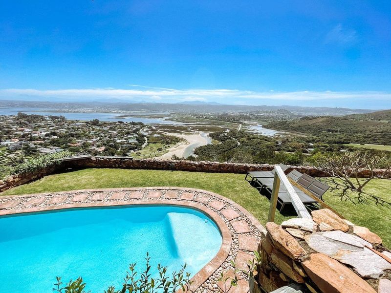 Outdoor pool area featuring a stone-edged swimming pool, manicured lawn, and a stone retaining wall with expansive panoramic views of the estuary and landscape.