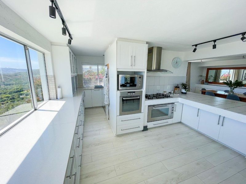 Modern kitchen featuring white cabinetry, built-in appliances, gas hob, and expansive countertops with scenic views and track lighting.