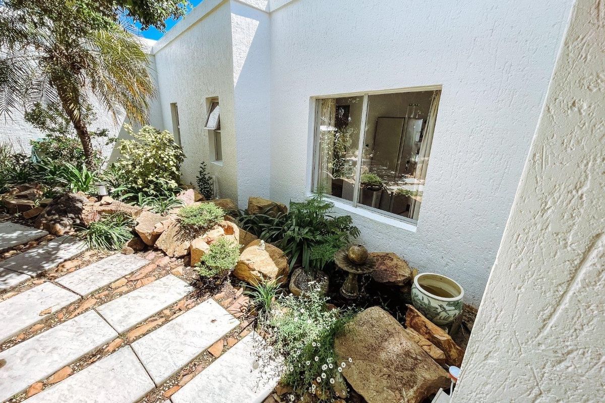 A well-maintained rear garden area featuring a paved walkway, rockery landscaping, and a clean white exterior facade with a large sliding window.