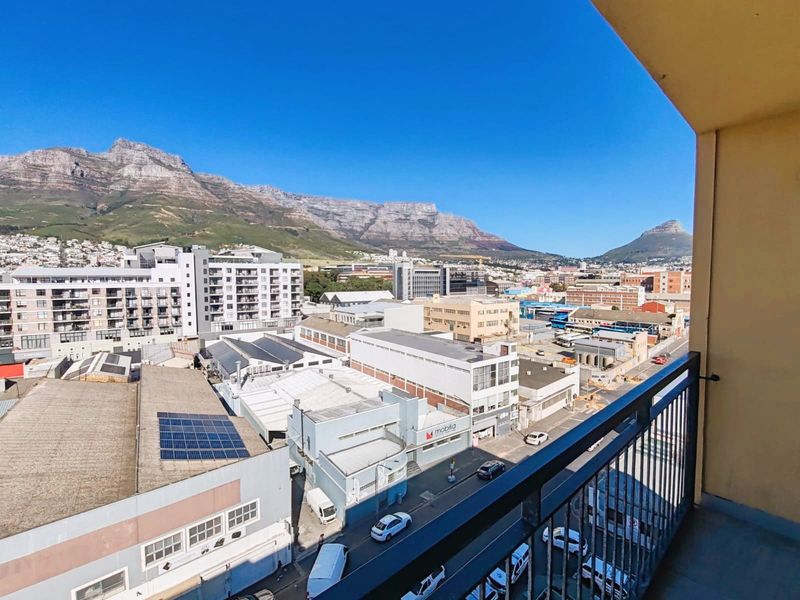 Elevated urban view from a balcony overlooking the city skyline with prominent mountain scenery in the background.