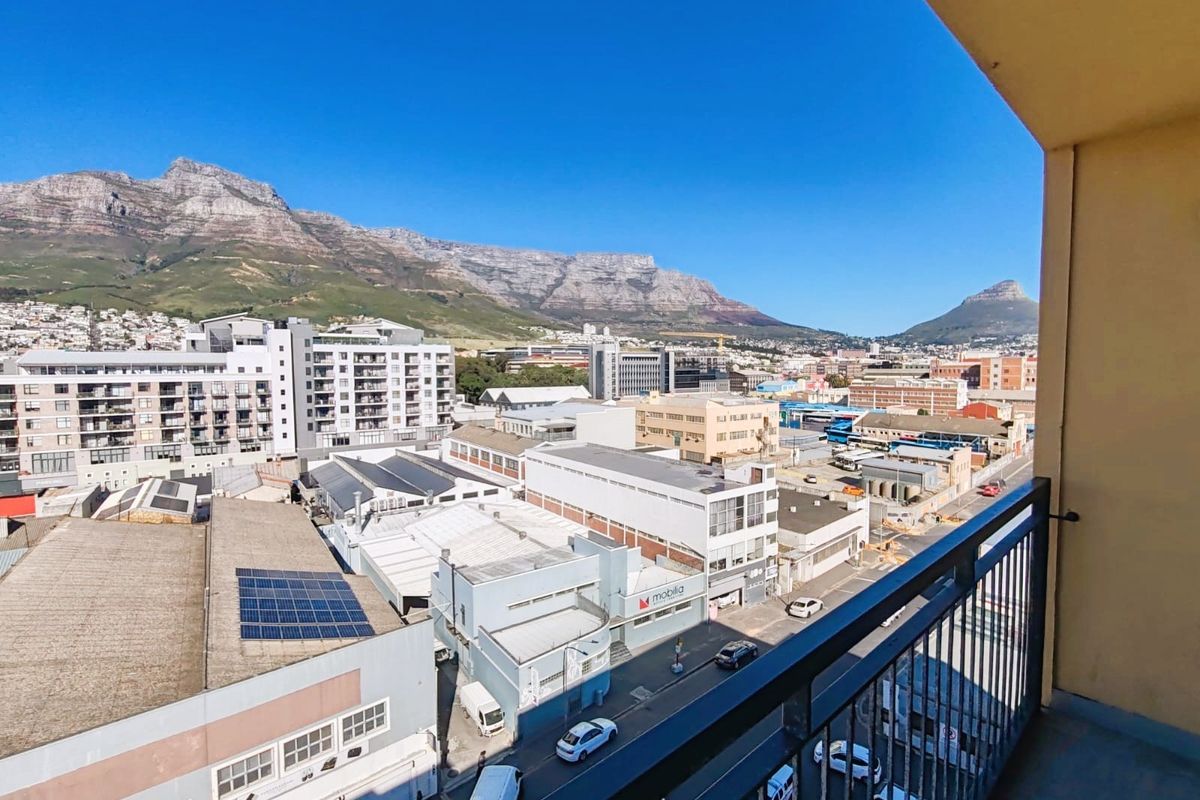 Elevated urban view from a balcony overlooking the city skyline with prominent mountain scenery in the background.