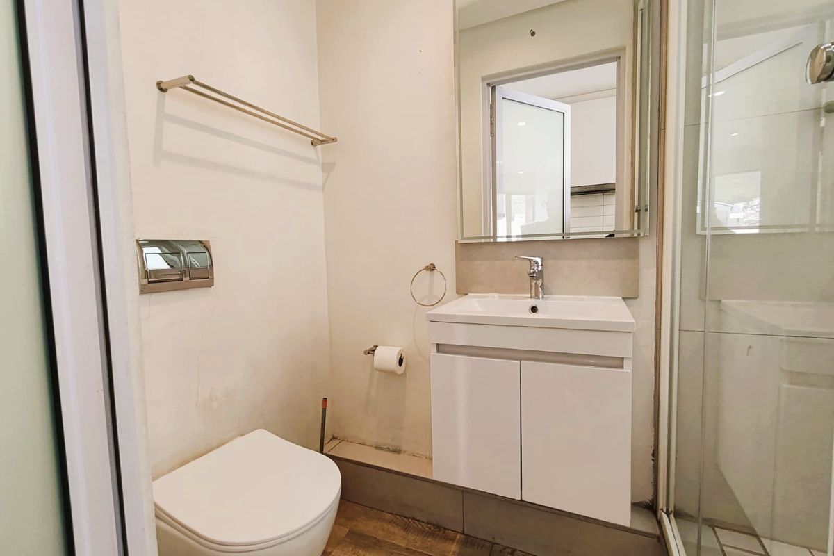 A compact, modern bathroom featuring a wall-mounted toilet, vanity basin, and a glass-enclosed shower with neutral tiled flooring.