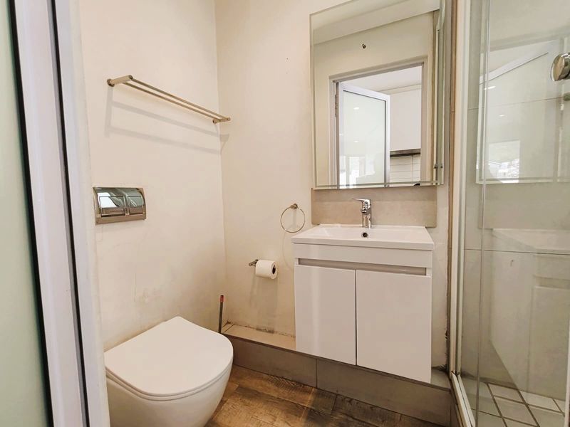 A compact, modern bathroom featuring a wall-mounted toilet, vanity basin, and a glass-enclosed shower with neutral tiled flooring.