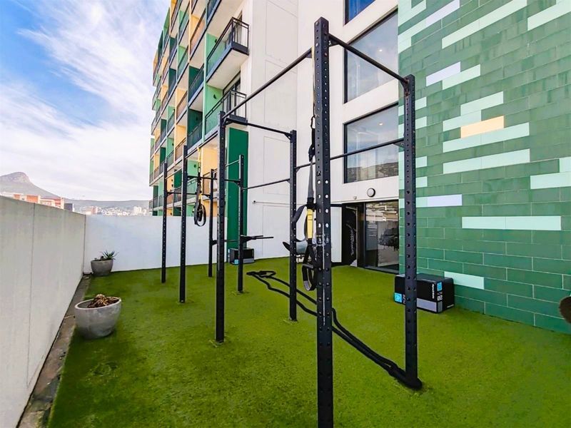 Outdoor gym area featuring a functional training rig installed on artificial turf, situated on a building terrace with modern tiled exterior finishes.
