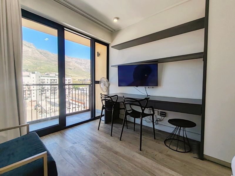 Modern bedroom featuring built-in desk and shelving, laminate flooring, and large sliding glass doors opening to a balcony with mountain views.