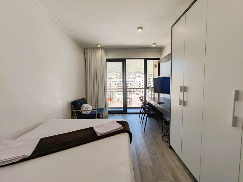 A modern bedroom featuring built-in wardrobes, laminate flooring, and direct access to a balcony with mountain views.