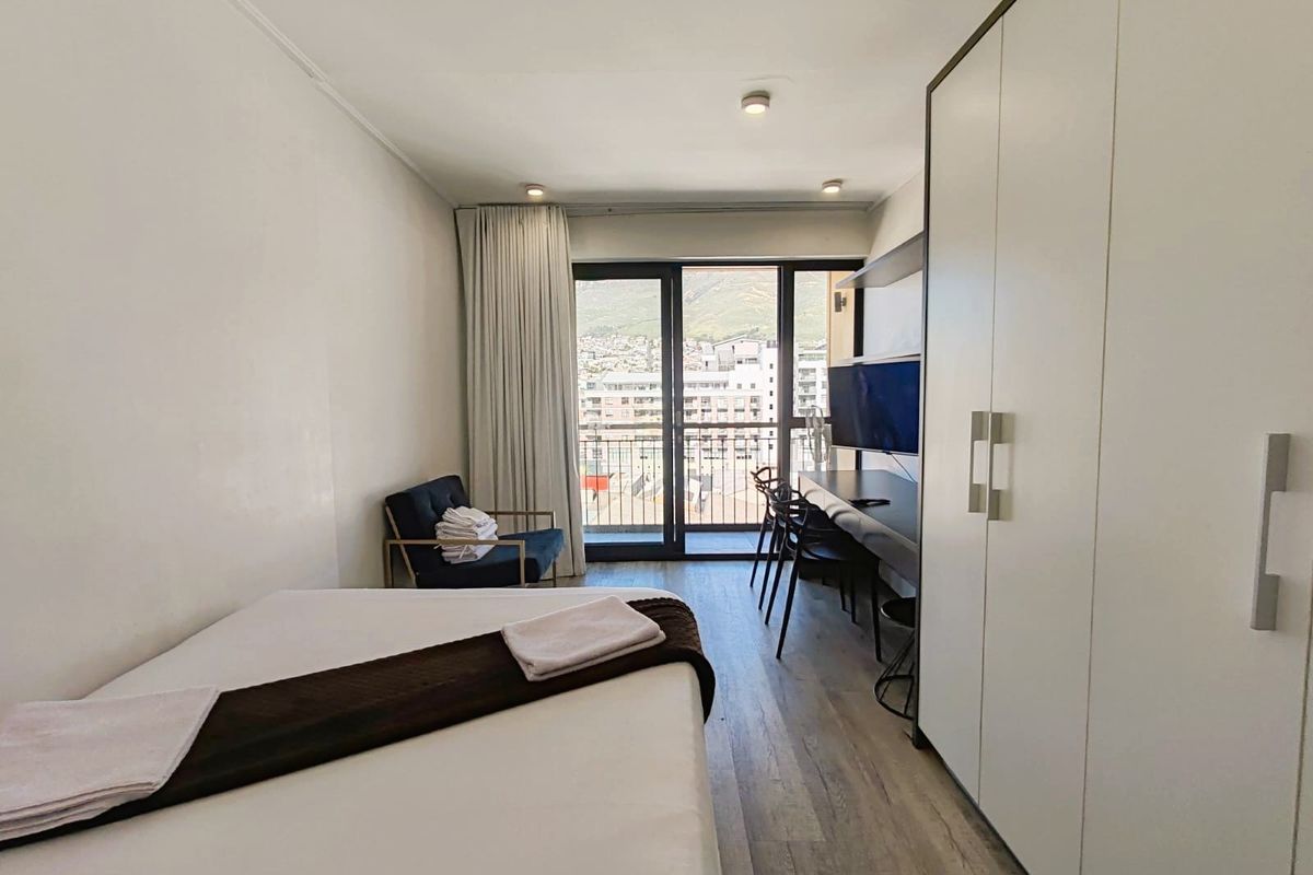 A modern bedroom featuring built-in wardrobes, laminate flooring, and direct access to a balcony with mountain views.