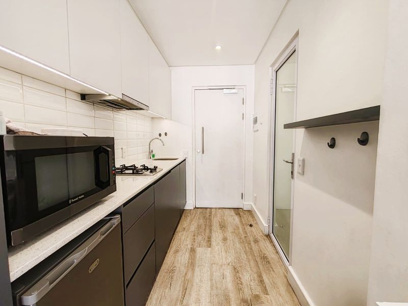 Modern galley-style kitchen featuring sleek two-tone cabinetry, stone countertops, subway tile backsplash, gas hob, and integrated extractor fan with under-cabinet lighting.