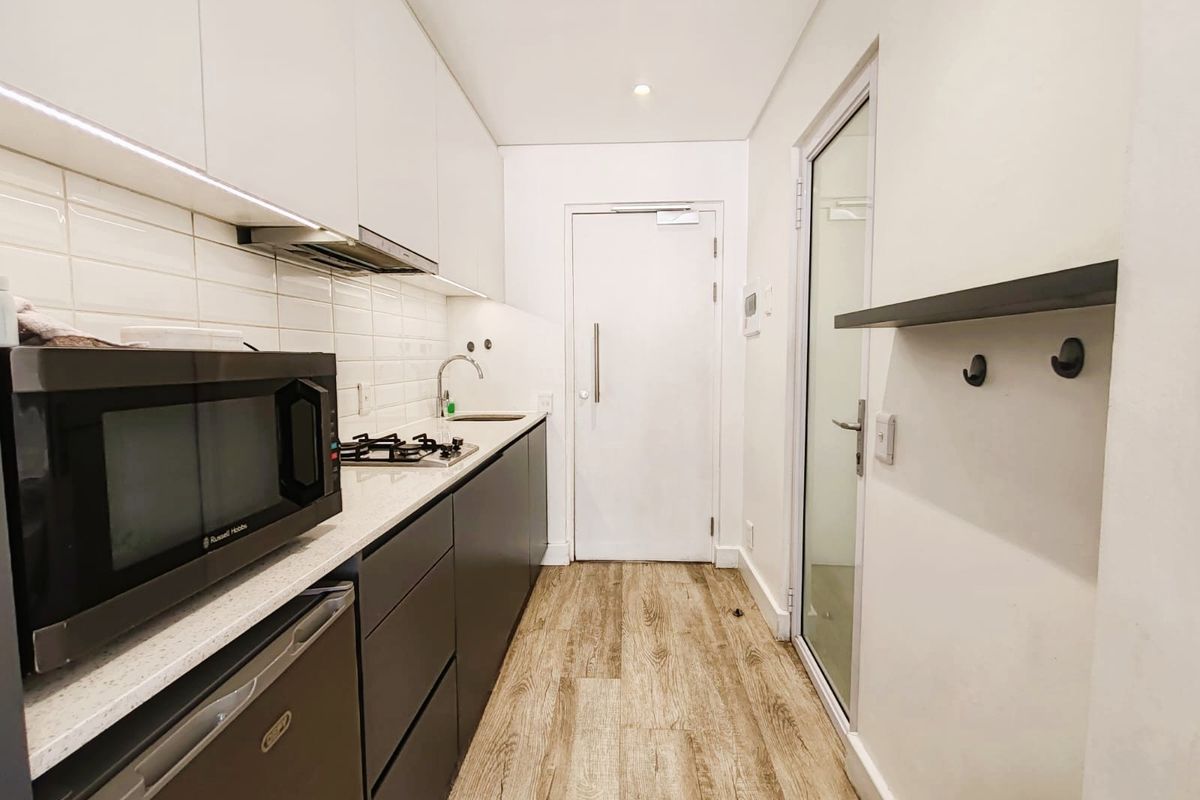 Modern galley-style kitchen featuring sleek two-tone cabinetry, stone countertops, subway tile backsplash, gas hob, and integrated extractor fan with under-cabinet lighting.