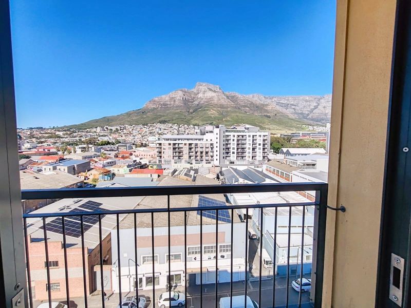 Elevated urban view overlooking the surrounding cityscape with a prominent mountain backdrop, framed by a balcony railing.