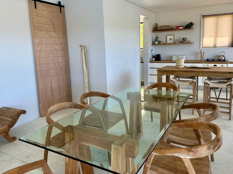 Modern open-plan living and dining area featuring polished concrete floors, a sliding barn door, and a functional kitchen with timber shelving and gas hob.