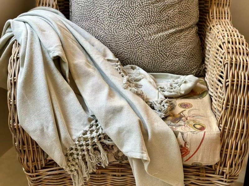 A close-up view of a wicker armchair with decorative cushions and a throw blanket.