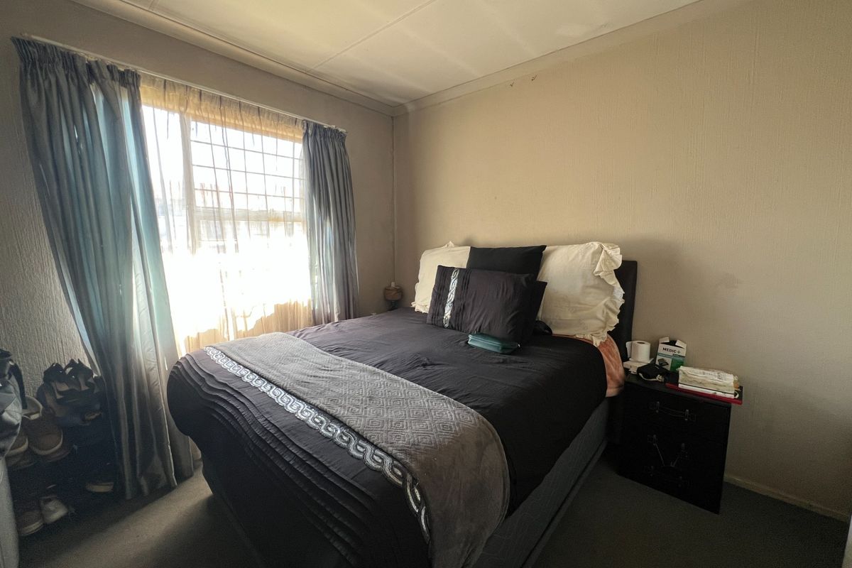A compact bedroom featuring carpeted flooring, coved ceilings, and security bars on the window, requiring cosmetic updates to improve the overall aesthetic.