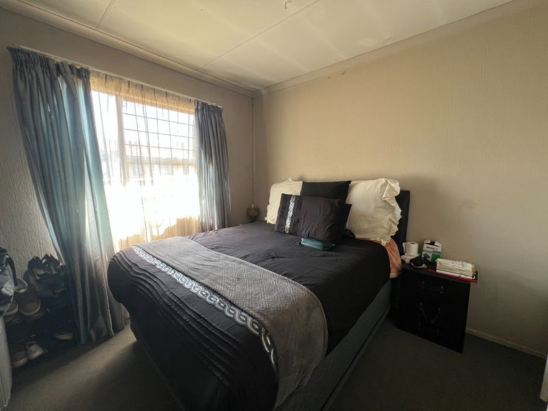 A compact bedroom featuring carpeted flooring, coved ceilings, and security bars on the window, requiring cosmetic updates to improve the overall aesthetic.