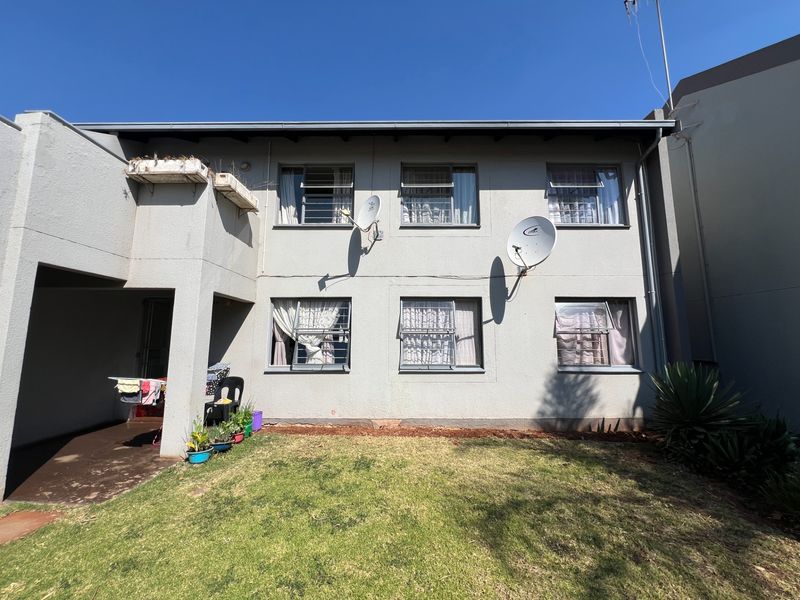 Rear view of the apartment building featuring a small private lawn, concrete patio area, and multiple windows with security bars.