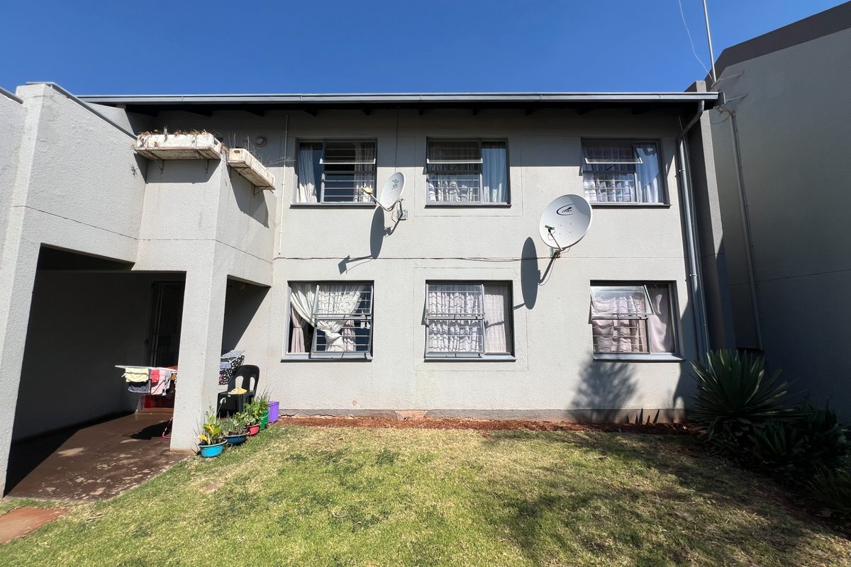 Rear view of the apartment building featuring a small private lawn, concrete patio area, and multiple windows with security bars.