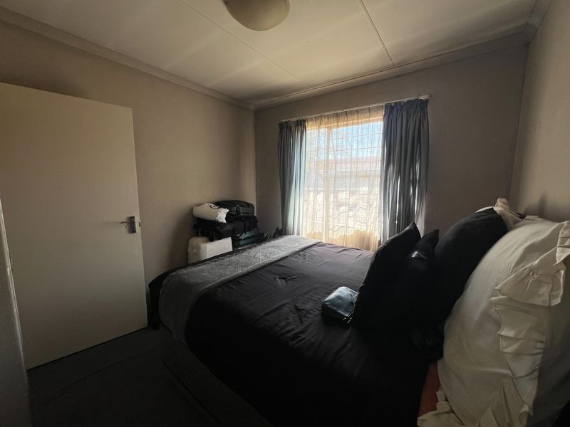 A standard bedroom featuring a built-in cupboard and security bars on the window, providing a functional and secure living space.