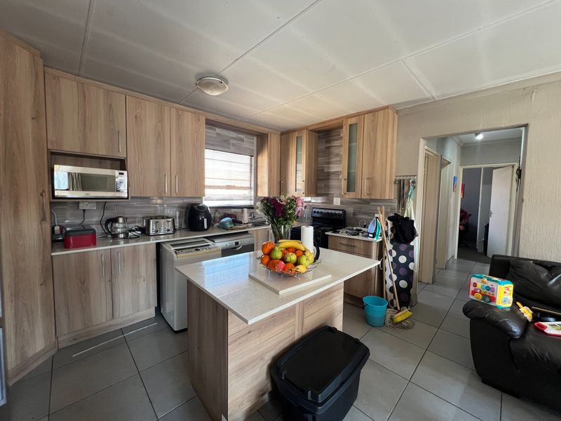Functional kitchen featuring light wood-look cabinetry, stone countertops, a central island, and tiled flooring, offering a practical layout for daily meal preparation.