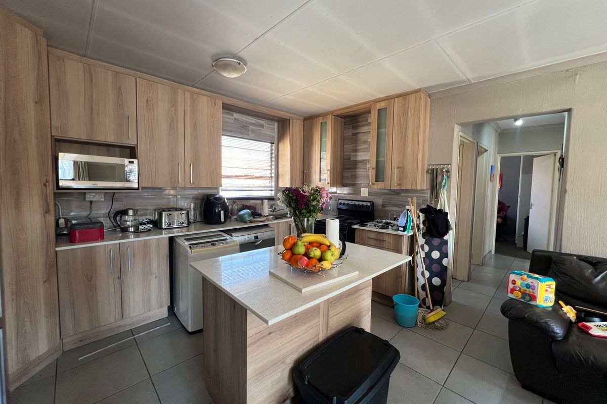Functional kitchen featuring light wood-look cabinetry, stone countertops, a central island, and tiled flooring, offering a practical layout for daily meal preparation.