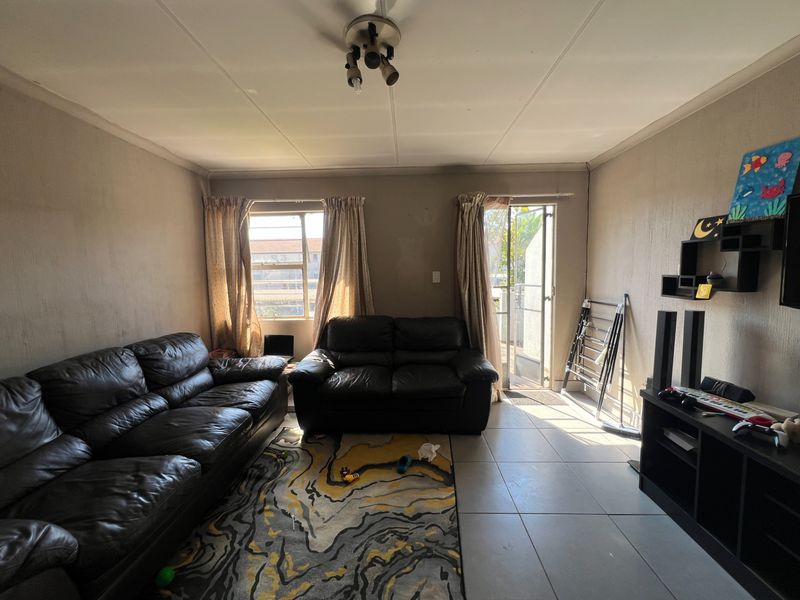 A living room featuring tiled flooring, natural light from windows and a glass door, and neutral wall finishes.